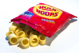 A box of 32 packets (34g each) of Hula Hoops Original by Hula Hoops, famous for their mega crunch and ring-shaped crisps, is shown open with snacks spilling onto a white surface.