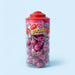 A clear plastic jar of Yirli ZOOM strawberry candy with a red lid, filled with pink and red foil-wrapped lollipops, set against a light blue background.